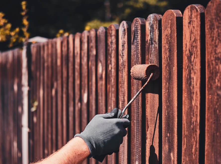 Man in protective gloves is painting a wooden fence on a bright summer day